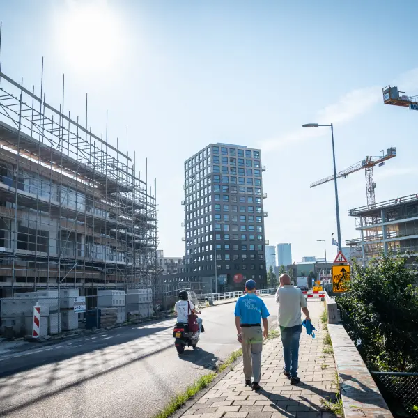 Mensen lopen over straat met op de achtergrond bouwprojecten en hijskranen.