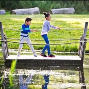 Twee kinderen spelen op een houten bruggetje in de natuur.