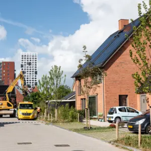 Foto van een woonwijk met enkele auto's en hoogbouw op de achtergrond.