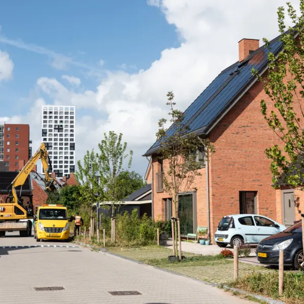 Foto van een woonwijk met enkele auto's en hoogbouw op de achtergrond.