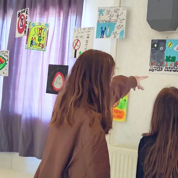 Twee kinderen kijken naar tekeningen van klasgenoten over roken en rookvrij.