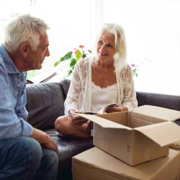 Vitale seniore man en vrouw zitten op de bank; ernaast staat een aantal verhuisdozen.