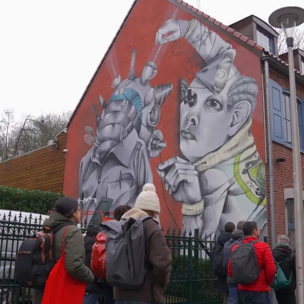 Een groep mensen loopt langs een woonhuis met op de zijkant een drie verdiepingen-hoog street-artwerk van kunstenaar Claudio Ethos.