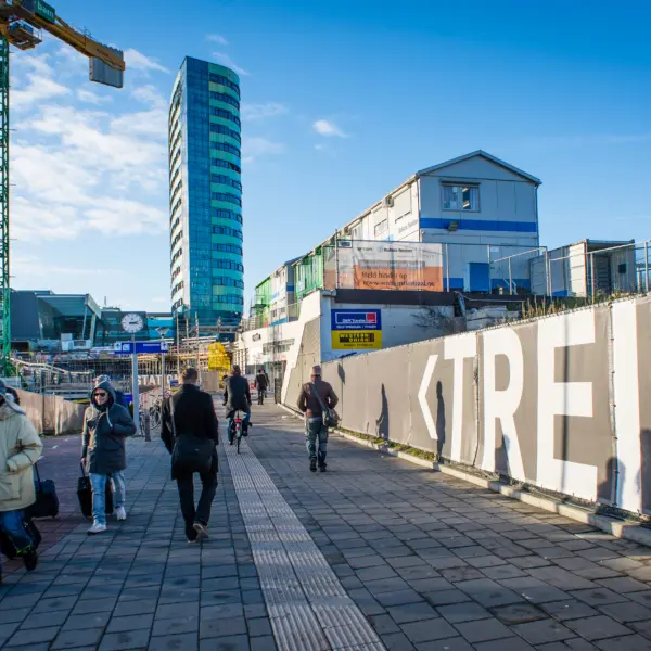 Gebiedsontwikkeling rond een station met nieuwbouw, bouwkranen en reizigers.