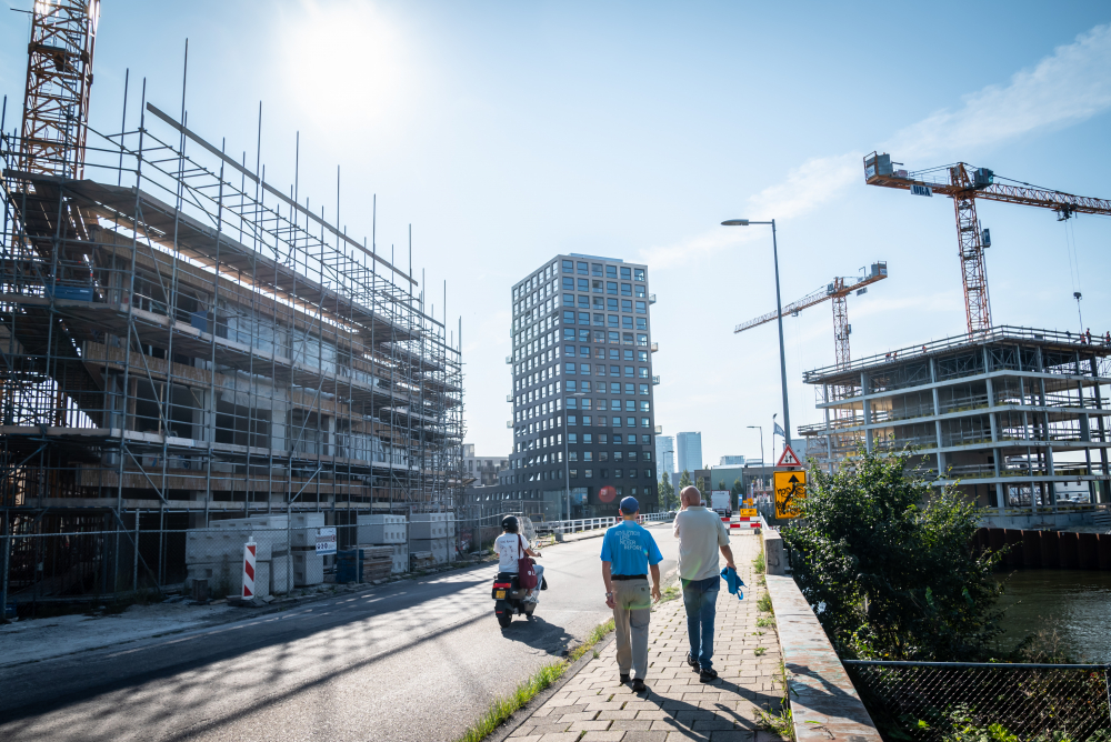 Mensen lopen over straat met op de achtergrond bouwprojecten en hijskranen.