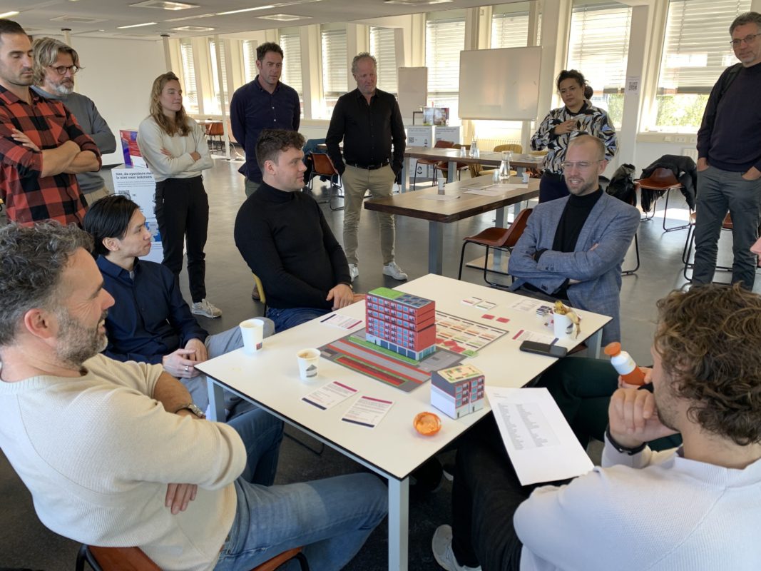 Spelers van de serious game ‘Afwegen van belangen bij optoppen’ zitten rond de tafel en spelen het spel.