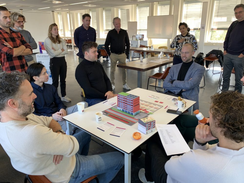 Spelers van de serious game ‘Afwegen van belangen bij optoppen’ zitten rond de tafel en spelen het spel.