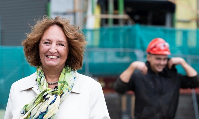 Foto van Liesbeth Spies met op de achtergrond een man met een bouwhelm.